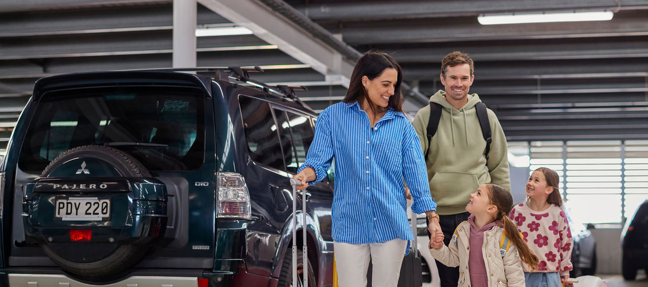 mum dad and two daughters get ready for a holiday and walk through the car park to ward the terminal to check in for their family aeroplane flight